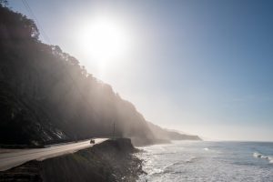 海岸に続く尾根の上に太陽が輝いている。遠くでは車が道を走っている。